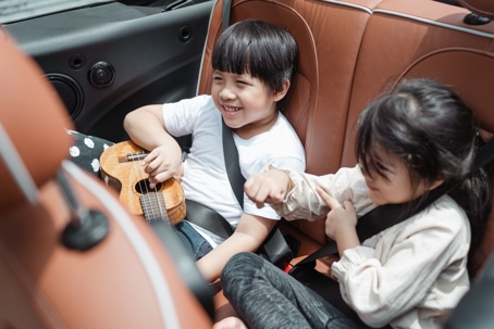 Two small children wearing seat belts and sitting in the back of a car.